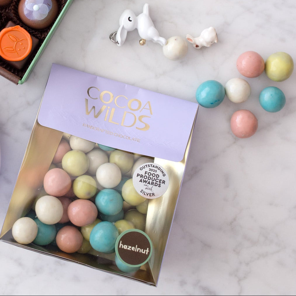Assorted chocolates including a bunny-shaped chocolate, a box of truffles, and a small bag of pastel candies on a marble surface.