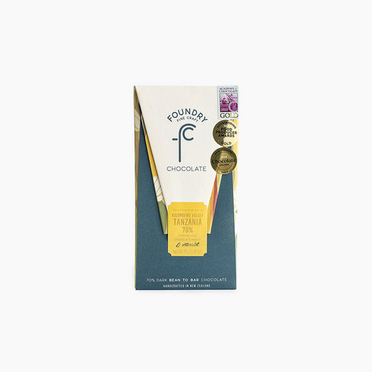A packaged Foundry brand dark chocolate bar with the label showing 'Single Origin Tanzania 70% Dark Chocolate'. The packaging is primarily white and blue with a chocolate color section showing the texture and brand name.